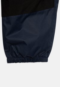 Mörkblått, lättviktigt tyg med en jämn textur; har en elastisk mudd och en kontrasterande svart panel överst.