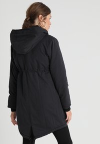 Svart lang dunjakke med hette, elastisk midje og sidelommer. Smidig stoff og en lett innsvingt silhuett i kanten.