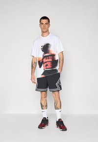 White graphic t-shirt with a blurred basketball player in red and black, paired with black shorts featuring white accents and a patterned texture.