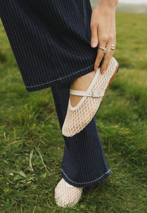 Hånd justerer flad mesh sko med spænde, båret med mørkeblå koksbuks på græsbaggrund.