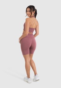 Gekromde, atletische set in een gedempte rozenkleur, bestaande uit een cropped top en hoogwaardige shorts van rekbare stof; gecombineerd met witte sneakers.