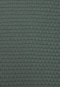 Dunkelgrüner gestrickter Stoff mit einer strukturierten Oberfläche, die eine Reihe von kleinen, einheitlichen Stichen aufweist.