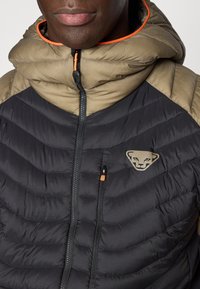 Μπουφάν με επένδυση σε μαύρο και χακί χρώμα. Διαθέτει ψηλό γιακά, ολόκληρο φερμουάρ, λογότυπο στο στήθος και αντιθετικές πορτοκαλί λεπτομέρειες.