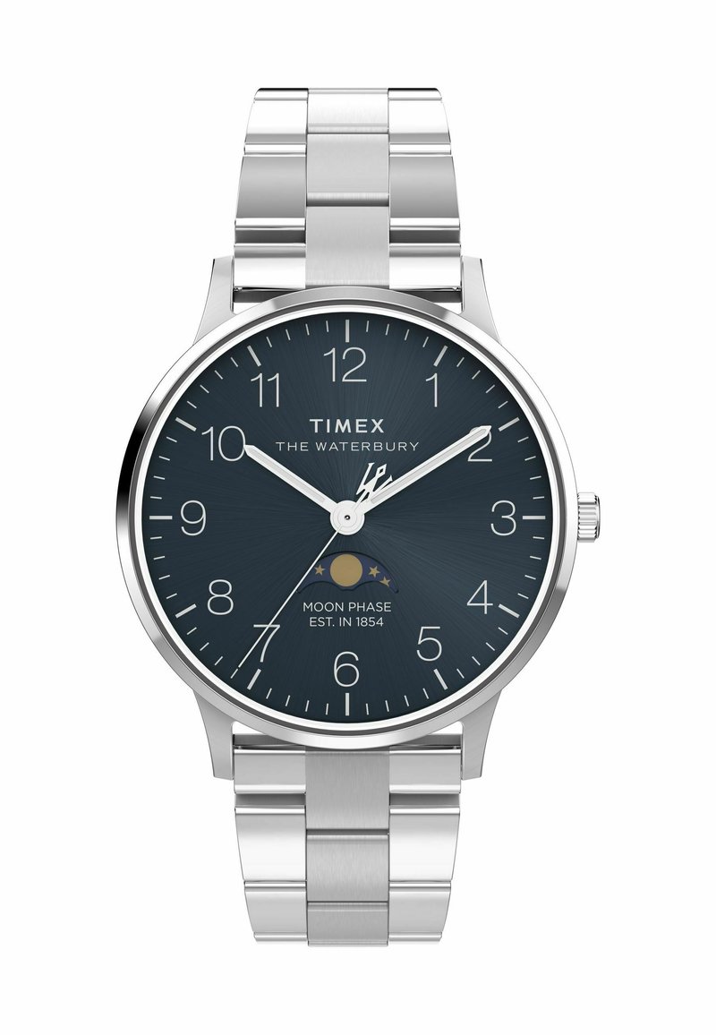 Montre Timex Waterbury avec bracelet en acier inoxydable argenté, cadran bleu marine, index blancs et indicateur de phase lunaire. Design de boîtier circulaire.