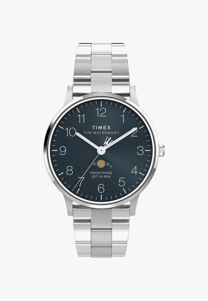 Montre Timex Waterbury avec bracelet en acier inoxydable argenté, cadran bleu marine, index blancs et indicateur de phase lunaire. Design de boîtier circulaire.