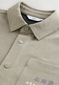 Gray collared shirt made of textured fabric, featuring a concealed button placket, green buttons, and embroidered accents on the front.