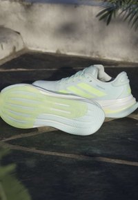 Baskets de sport bleu clair avec une semelle jaune-vert. Tige en mesh lisse, système de laçage et trois bandes verticales sur le côté.