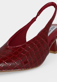 Talons slingback rouges avec motif crocodile texturé brillant et bout pointu, dotés d'un talon bloc bas et d'une étiquette de marque visible à l'intérieur.