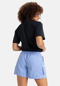 Camisa negra de manga corta combinada con pantalones cortos elásticos de cintura alta en azul claro, que cuentan con bolsillos de estilo cargo y un acento amarillo en contraste.