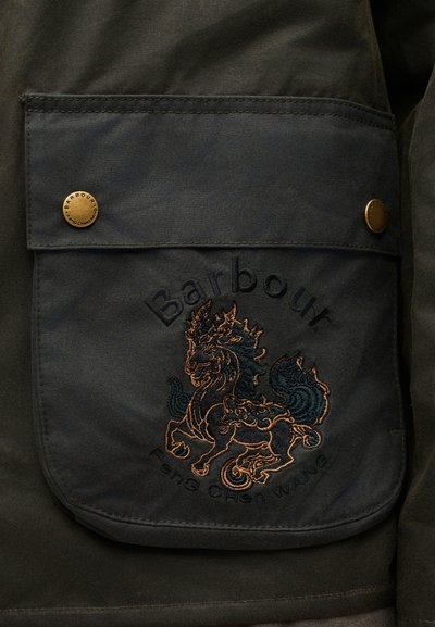 Σκοτεινή υφασμάτινη τσέπη με χρυσά κουμπώματα, κεντητό μυθικό πλάσμα και κείμενο "Barbour Feng Chen Wang" σε εξωτερικό ένδυμα.