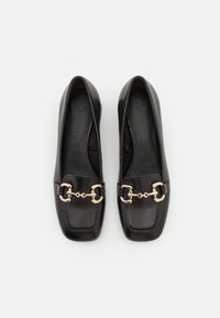Black leather flat shoes with a square toe design, featuring a gold chain accent over the instep and smooth, reflective texture.