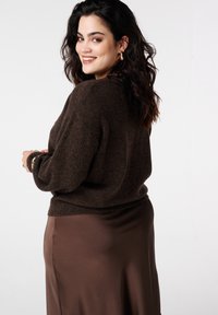 Bruin gebreide trui met een losse pasvorm, geribbelde manchetten en een cropped zoom, gecombineerd met een lange, gladde, donkerbruine satijnen rok.