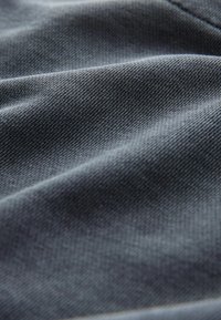 Tessuto grigio scuro con una sottile trama testurizzata, che mostra morbide pieghe e variazioni nelle riflessioni della luce, tipico dei tessuti intrecciati.