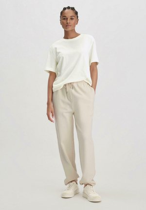 Lichtgele katoenen t-shirt met een losse fit, gecombineerd met beige taps toelopende joggers met een elastische tailleband en boorden. Witte sneakers.