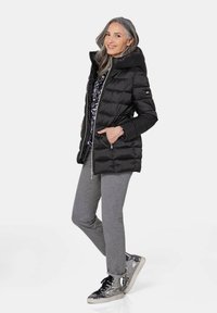 Schwarze Steppjacke mit hohem Kragen, Reißverschluss und zwei Seitentaschen. Sie verfügt über horizontale Steppungen und ein elegantes, schlankes Design.