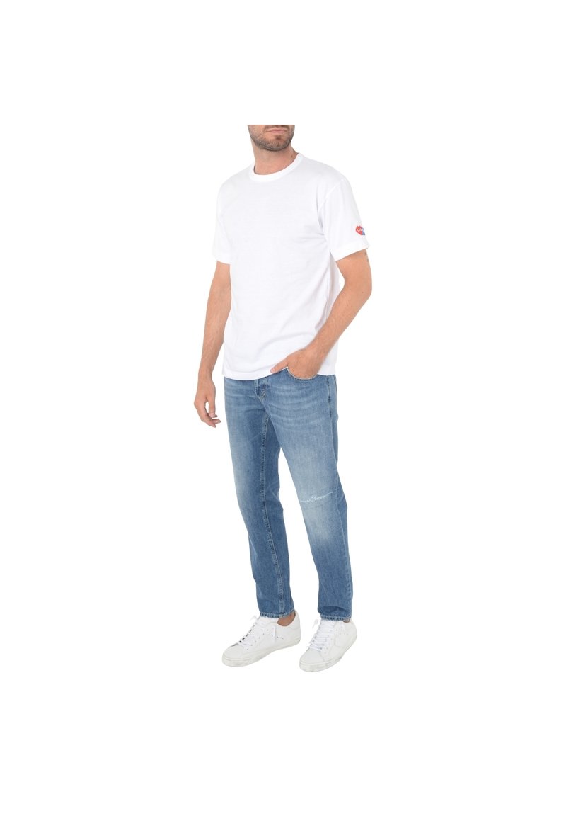 T-shirt bianca a maniche corte con colletto tondo e logo rosso sulla manica, abbinata a jeans in denim azzurro chiaro e sneakers bianche.