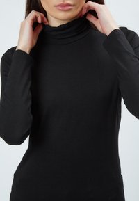 Schwarzes Rollkragenoberteil aus weichem, elastischem Stoff. Verfügt über lange Ärmel und ein figurbetontes Design mit hohem Kragen. Glatte Textur.