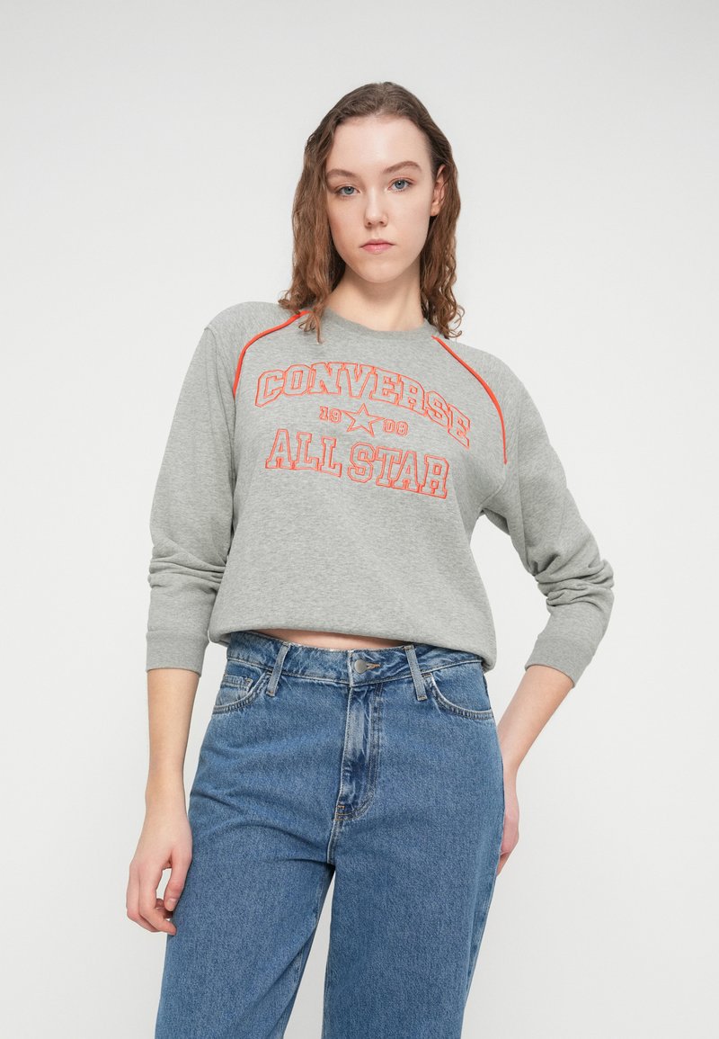 Grå cropped sweatshirt med røde detaljer og teksten "CONVERSE ALL STAR". Kombineret med højtaljede blå denimjeans. Blødt, afslappet stof.