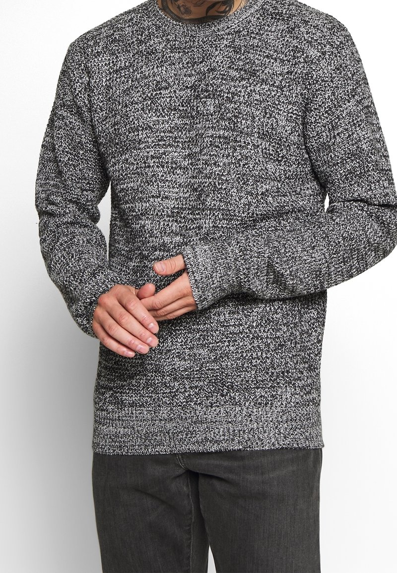 Šedý a černý pletený svetr s dlouhými rukávy, žebrovanými manžetami a kulatým výstřihem, zdobený texturovaným melanžovým vzorem.