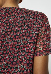 Tissu noir transparent avec un motif floral de fleurs rouges et de feuilles vertes. Manches courtes avec un col arrondi, texture douce.