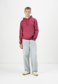 Maroon hoodie with front pocket and drawstring, paired with light wash straight-leg jeans and cream sneakers with rubber soles.