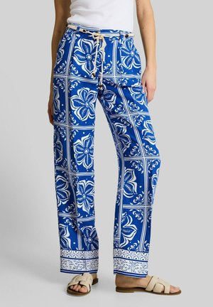 Pantalon ample à motif floral bleu et blanc avec ceinture en corde, porté avec des sandales blanches et un top blanc sans manches.