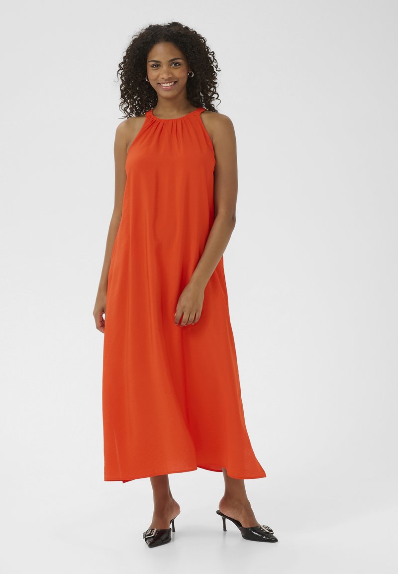 Abito maxi arancione senza maniche con scollatura arricciata e vestibilità ampia, abbinato a mules nere lucide con tacco. Design semplice e colore audace.