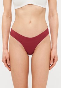 Burgundy bikiniunderdel med en smal, v-formad midja och minimal täckning. Slät material, sömlös design och ingen synlig hårdvara.