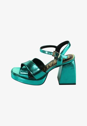 Tyrkysové metalické sandály na vysokém podpatku s širokým křížovým páskem, zapínáním kolem kotníku a čtveratým blokovým podpatkem, s lesklým povrchem a polstrovanou stélkou.
