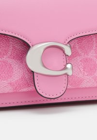 Gros plan d’un sac en cuir rose avec un fermoir argenté en forme de « C » et un panneau en tissu texturé cousu en dessous.