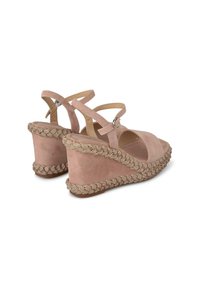 Sandali con zeppa in morbida suede rosa con cinturini incrociati alla caviglia. Il dettaglio in iuta intrecciata attorno al tacco a zeppa aggiunge texture e particolarità.