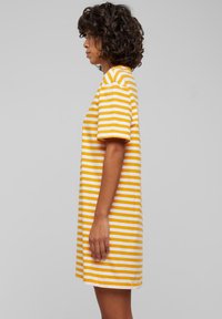 Robe t-shirt rayée avec des rayures horizontales jaunes et blanches, manches courtes, coupe décontractée et coupe droite, confectionnée dans un tissu doux.