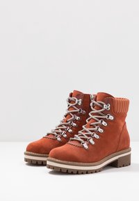 Las botas de senderismo de ante naranja cuentan con ojales plateados y cordones grises, un collar acolchado y una suela robusta para tracción.