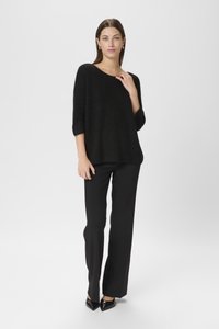 Melns pārspīlēts džemperis, kas izgatavots no mīkstas, teksturētas auduma, ar trīs ceturtdaļu piedurknēm, apvienots ar taisniem melniem biksēm un norādītiem melniem papēžiem.