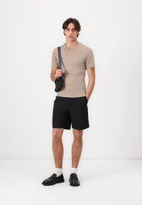 Beige t-paita, mustat shortsit, musta olkalaukku, mustat kengät, valkoiset sukat. Yksinkertainen muotoilu, sileä rakenne, rento pukeutuminen.