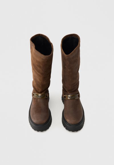 Καφέ δερμάτινες μπότες μέχρι το γόνατο με στυλ χαλαρής πτώσης, με μεταλλικό πόμολο και υφασμένο καουτσούκ στη σόλα.