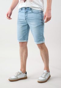Pantalones cortos de mezclilla azul claro con corte recto, dobladillos enrollados y un diseño clásico de cinco bolsillos, combinados con zapatillas blancas con detalles en gris.