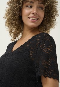 Black lace top featuring a v-neckline and short sleeves. The fabric displays floral patterns and a delicate scalloped hemline.