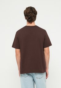 Camiseta de algodão castanha com gola redonda, mangas curtas e corte direito. Projetada para um ajuste descontraído, apresentando uma cor sólida sem padrões.