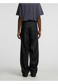 Tumši zili džinsa kravas bikses ar vaļēju piegriezumu, ar kabatām aizmugurē un šuvju detaļām, kombinētas ar īsām piedurknēm pelēku T-kreklu.