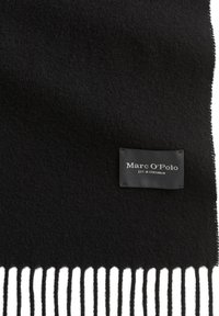 Écharpe en laine noire à texture douce, avec de longues franges et une petite étiquette noire portant le nom de la marque "Marc O'Polo" en blanc.