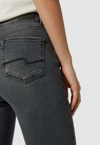 Dunkelgraue Jeans mit einem taillierten Design, das eine gewundene Taschennaht, eine glatte Textur und ein Etikett am Bund auf der Rückseite aufweist.