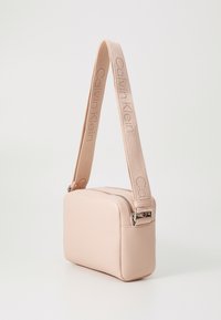 Borsa a tracolla in pelle rosa con forma rettangolare, texture liscia, chiusura con zip e tracolla beige con il logo Calvin Klein.