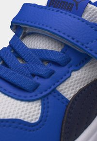 Κοντινό πλάνο μπλε και λευκού αθλητικού παπουτσιού Puma με πλέγμα ύφασμα, υφασμένους κορδόνια και λουράκι με βέλκρο στο πάνω μέρος.