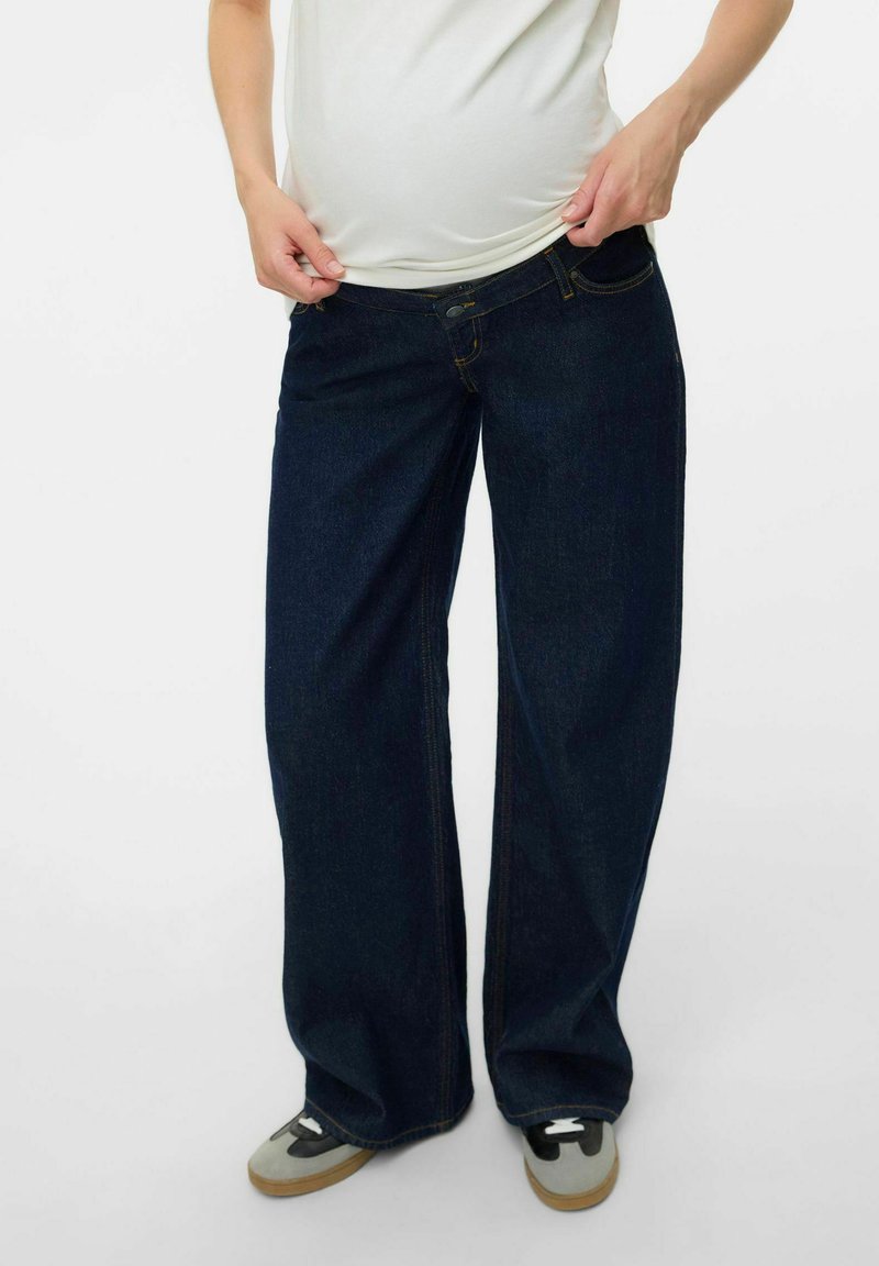 Dark blue wide-leg jeans in denim with yellow stitching, a button closure, and front pockets. Paired with gray sneakers.