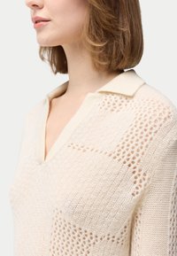 Strickpullover in Off-White mit V-Ausschnitt und Kragen; verfügt über strukturierte Muster und offene Strickdetails an den Ärmeln.