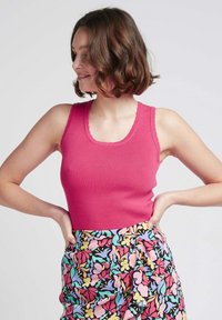 Débardeur rose ajusté en maille côtelée avec des bords festonnés, associé à une jupe à motifs floraux multicolores. La texture semble lisse et extensible.