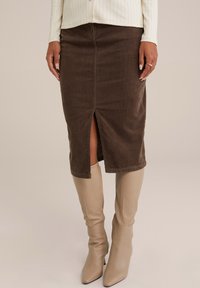 Fustă midi din corduroy maro cu o fanta frontală, având o textură netedă și un design ajustat, asortată cu cizme bej cu toc până la genunchi.