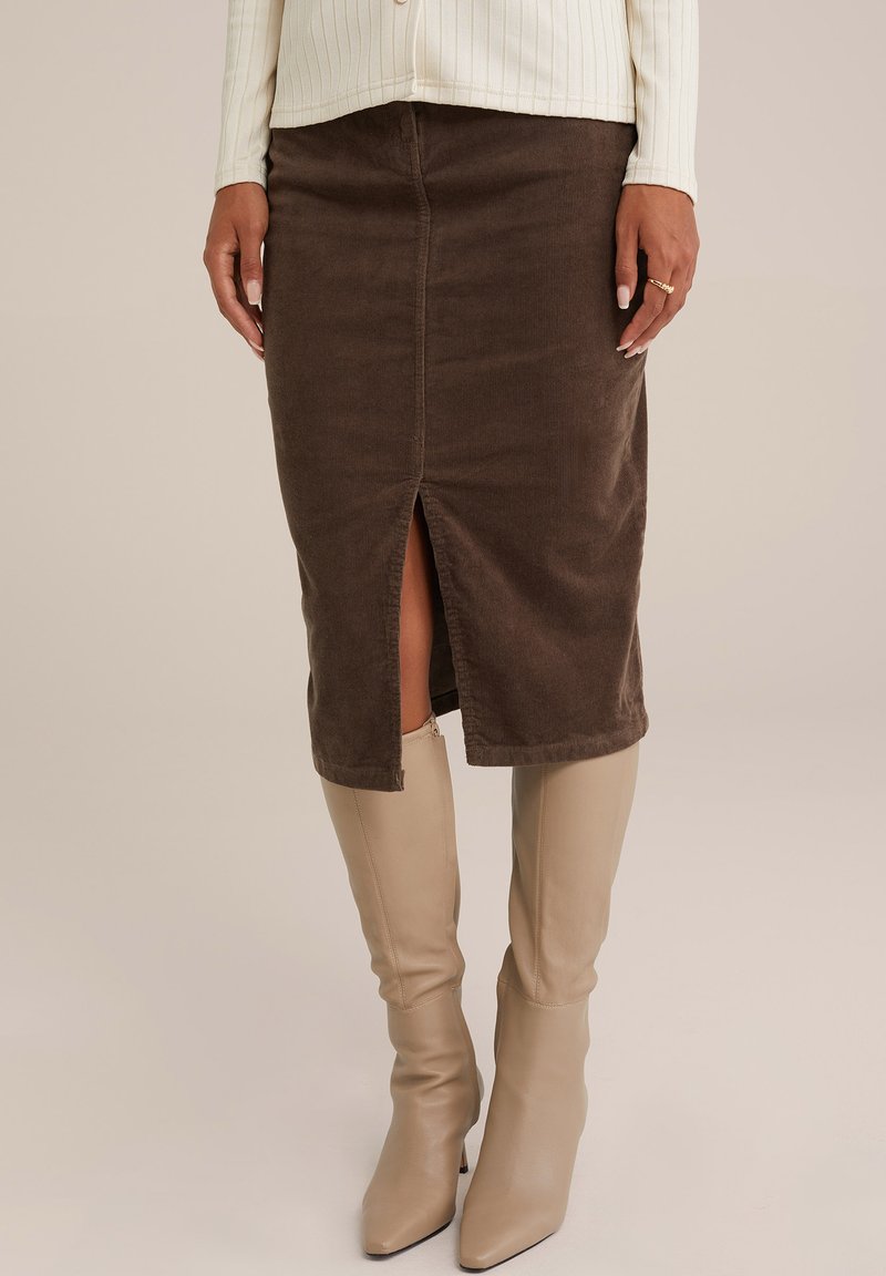 Fustă midi din corduroy maro cu o fanta frontală, având o textură netedă și un design ajustat, asortată cu cizme bej cu toc până la genunchi.
