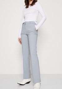 Jasnoszare spodnie w kant z prostymi nogawkami, z zamkiem błyskawicznym, kieszeniami bocznymi i gładką fakturą materiału. W zestawie z białą bluzką.